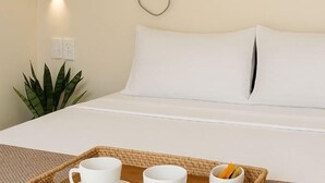 A neatly made bed with white linens, a bedside plant, and a tray with two cups and a bowl. - Sunrise Beach Resort (Santa Fe)