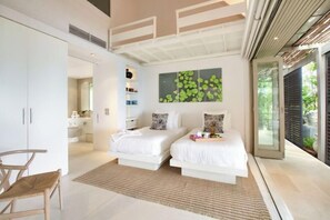 A modern bedroom with two beds, a large window, and a view of greenery. - The Headland Villa 2 (Koh Samui)