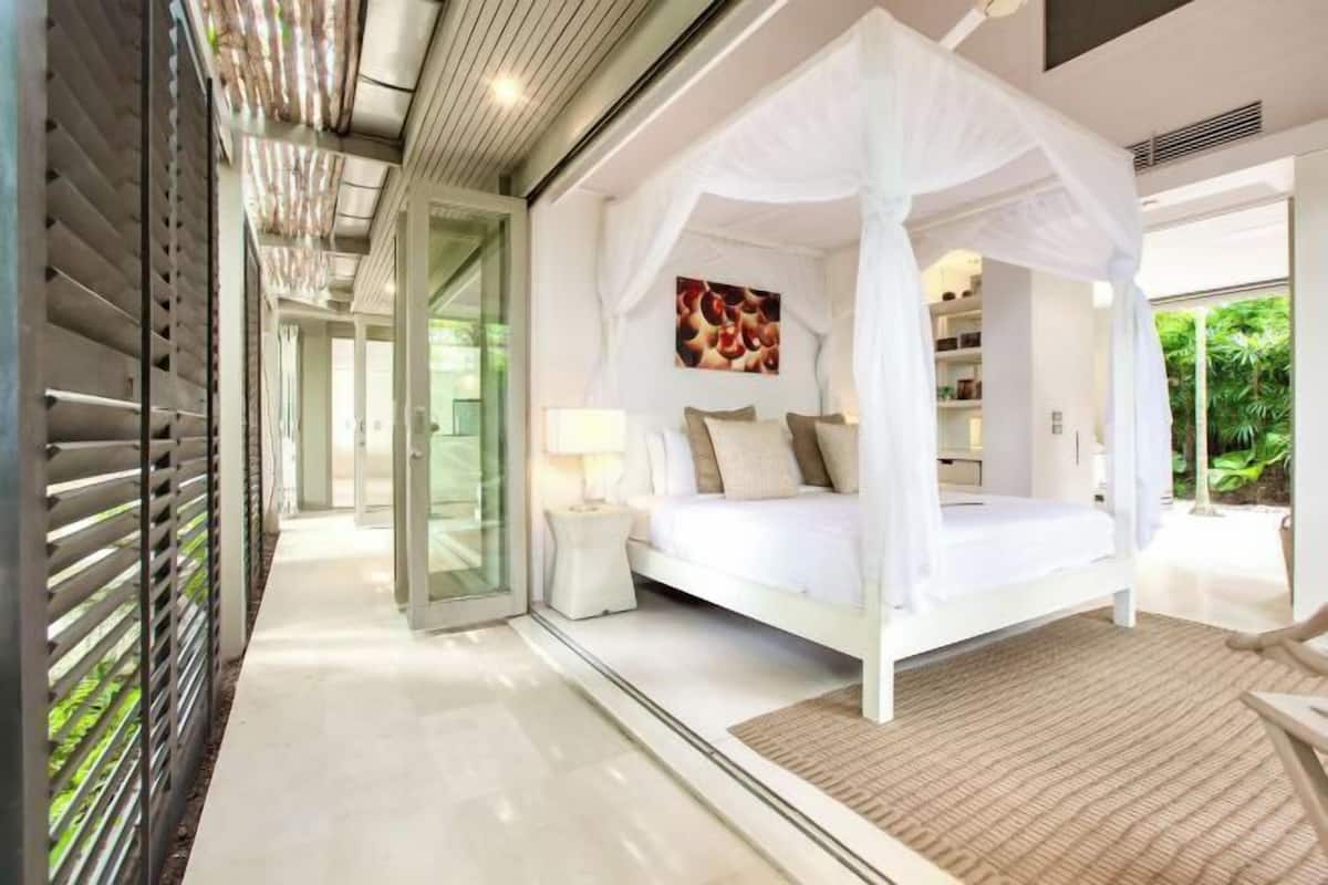 A modern bedroom with a canopy bed, a glass door leading to a balcony, and a view of greenery.