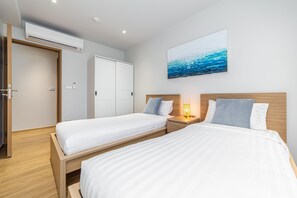 Een hotelkamer met twee enkele bedden, een houten hoofdbord, een nachtkastje met een lamp en een schilderij van de oceaan aan de muur.