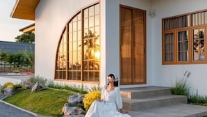 Una casa moderna con ventanas amplias, un camino de piedra y una persona sentada en los escalones.
