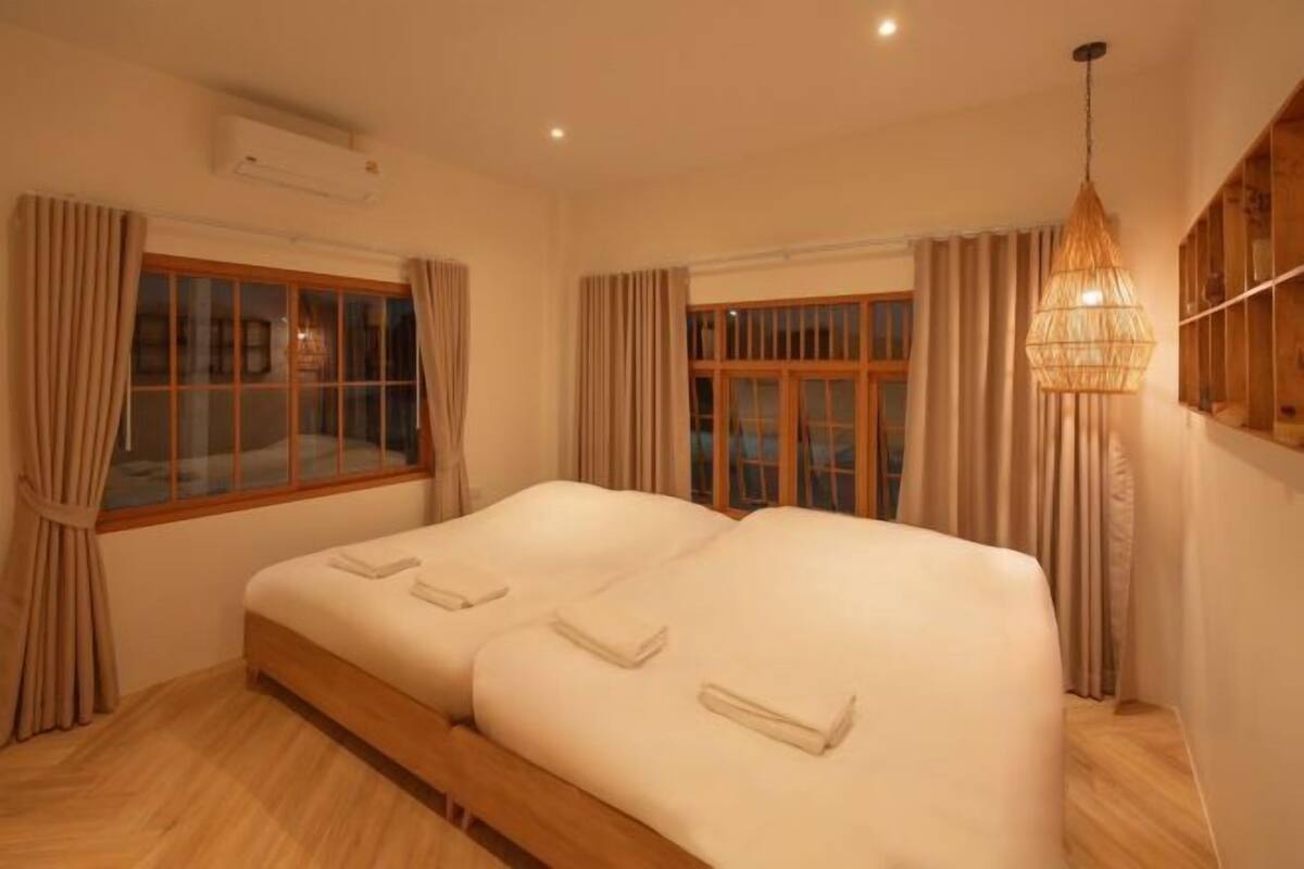 Una habitación con una cama grande, cortinas, un ventanal y una lámpara colgante.