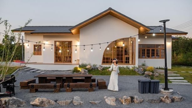 Una casa moderna con un patio de piedra, bancos de madera y luces colgantes.