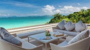 A sunlit outdoor seating area with wicker furniture, a glass coffee table, and a view of the ocean. - Ocean's 11 Villa (Phuket)