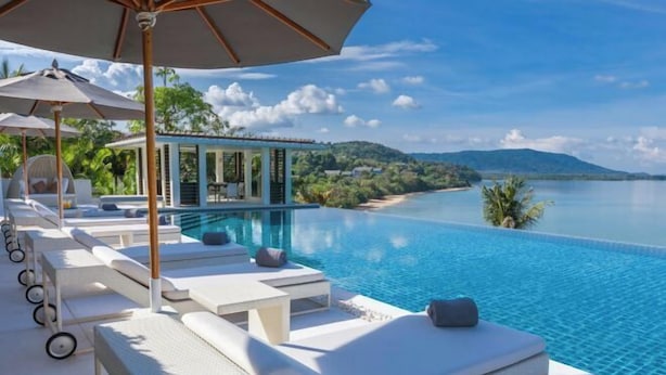 A poolside area with lounge chairs and umbrellas, overlooking a clear blue pool and a scenic view of a beach and hills. - Ocean's 11 Villa (Phuket)