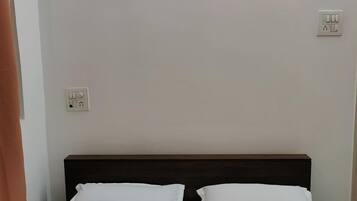 A bedroom with a bed, white pillows, a dark headboard, a painting of a night sky, and a power outlet on the wall.
