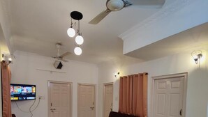Uma sala de estar com área de jantar, sofá, televisão e ventiladores de teto.