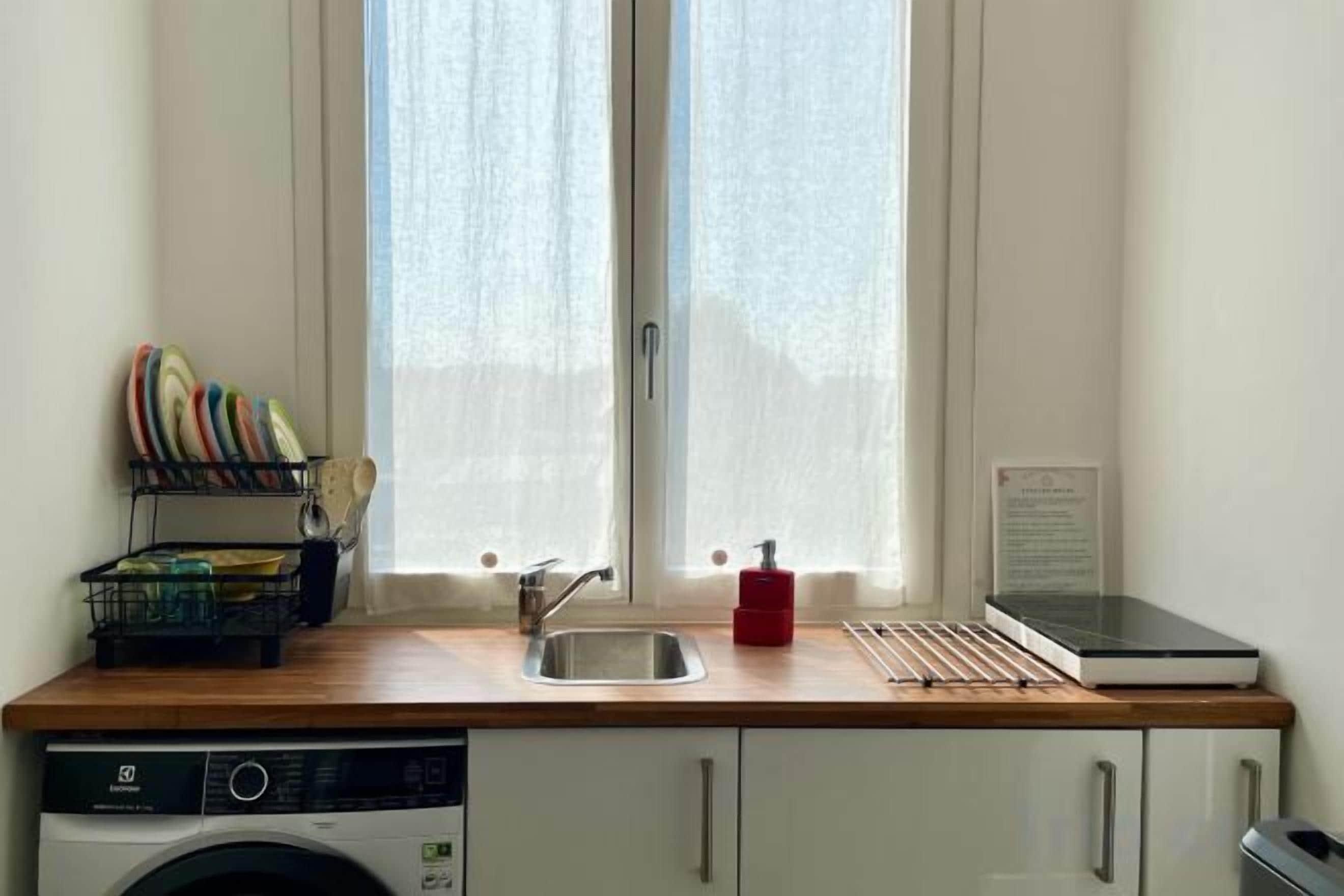 A kitchen with a washing machine, a sink, and a window with curtains.