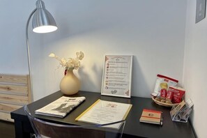 Ein Empfangstresen mit einer Blumenvase, einer Lampe, einer gerahmten Speisekarte und einigen Broschüren.