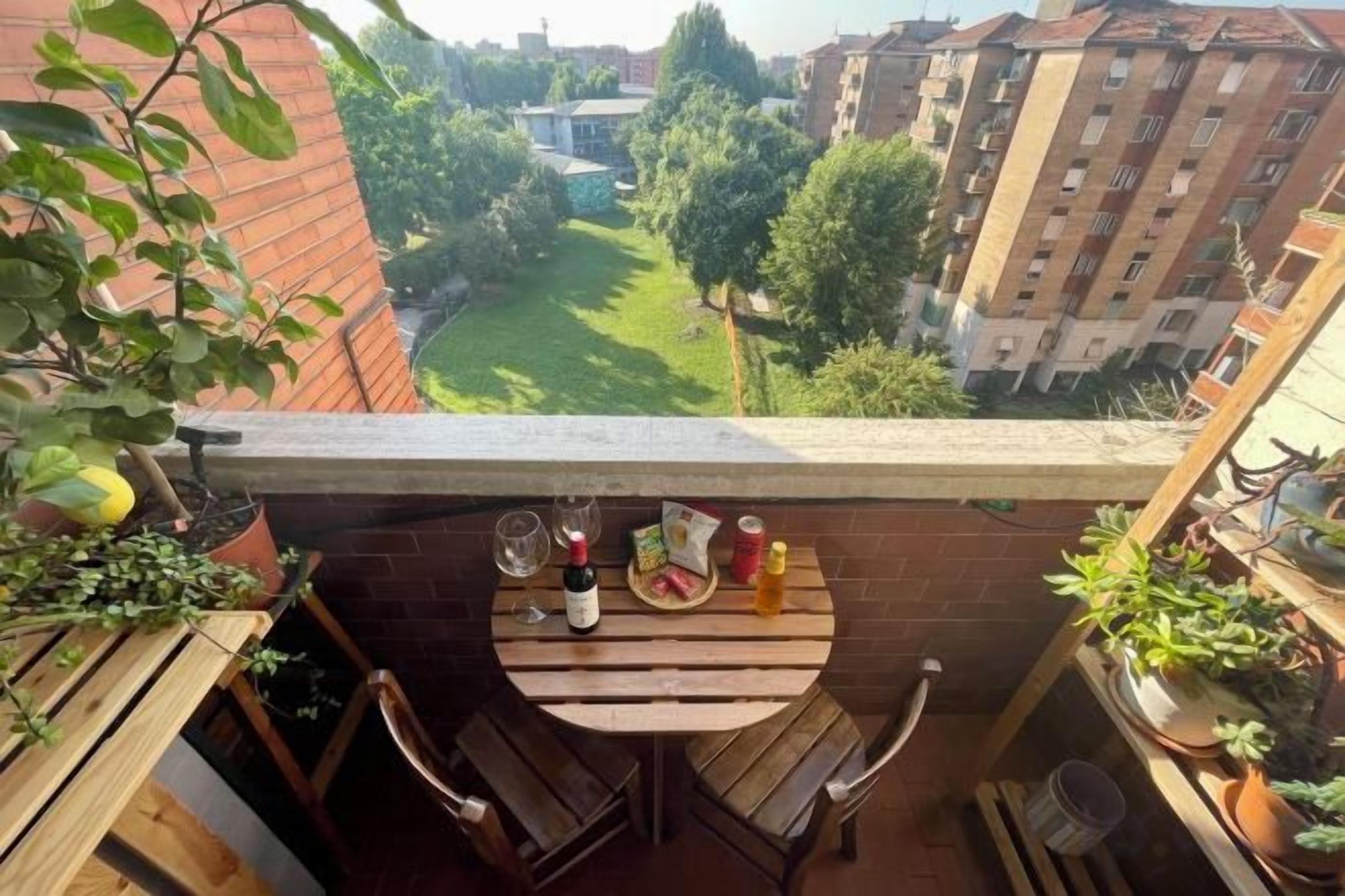 A balcony with a small table and chairs, overlooking a green courtyard and residential buildings.