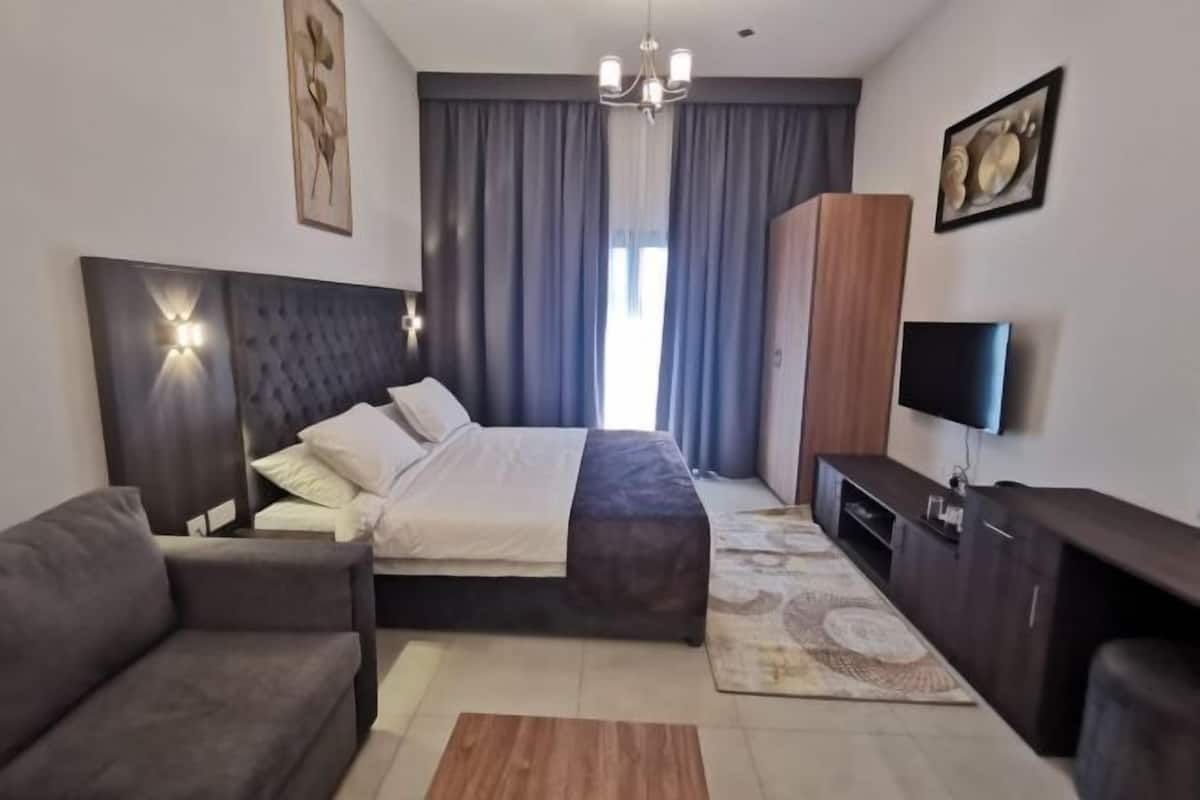 Ein modernes Schlafzimmer mit einem großen Bett, einer Couch, einem Fernseher und einem Holzkasten.