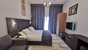 A modern bedroom with a large bed, a sofa, a TV, and a wooden cabinet.