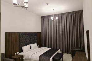 Una habitación de hotel moderna con una cama grande, cabecera de madera, una mesita de noche y un banco.