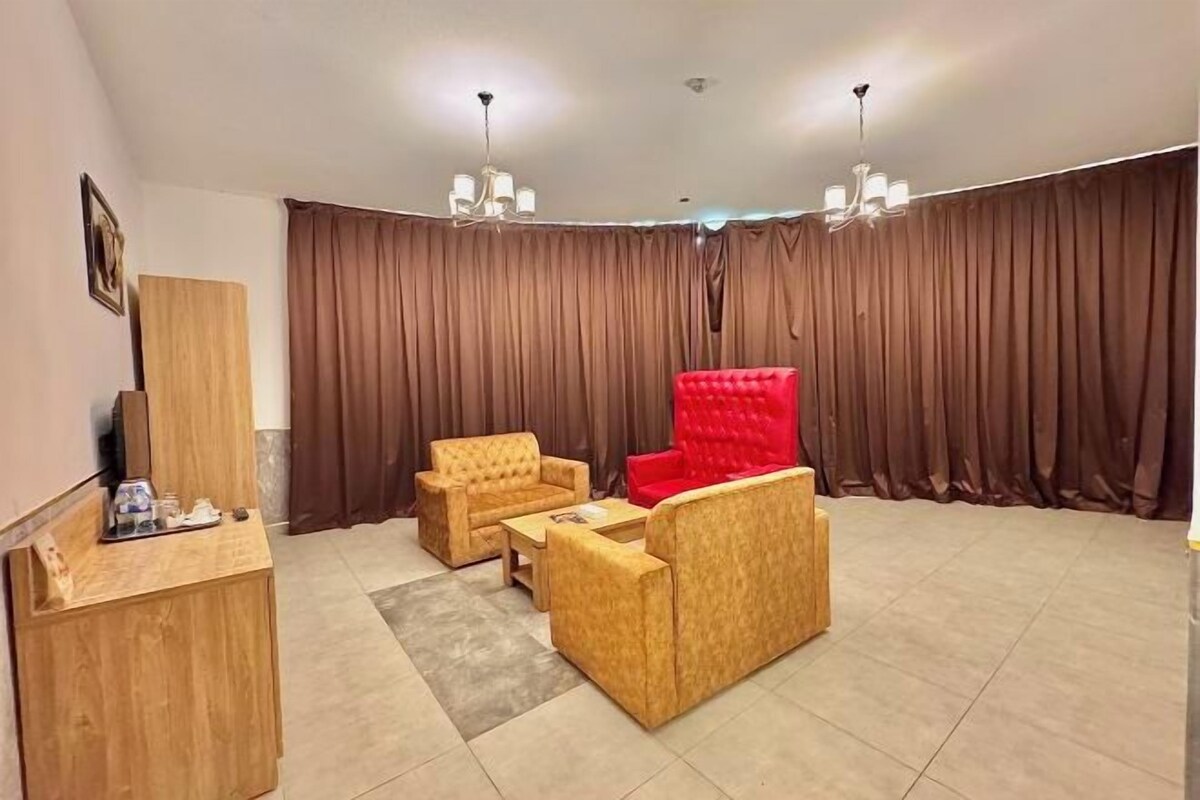 A room with a wooden desk, two armchairs, a red sofa, and a large curtain backdrop.