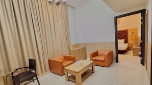 A modern hotel room with a wooden bed, two orange sofas, a glass table, and a dark chair.