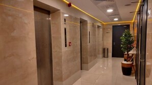 A modern elevator area with marble walls, a potted plant, and a fire extinguisher.