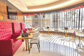 Un restaurant avec des sièges rembourrés de tissu rouge, une salle à manger avec des parois vitrées et une vue dégagée grâce à de grandes fenêtres.