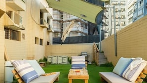 A courtyard with two wooden lounge chairs, a small table, and a green lawn. - Netanya Beach & Pool Elegant Studio (Netanya)