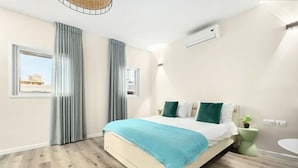 A bedroom with a bed, curtains, a window, a bedside plant, and a wall-mounted air conditioner. - Netanya Beach & Pool Elegant Studio (Netanya)