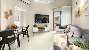 A modern living room with a flat-screen TV, a dining area with a table and chairs, a sofa, and a window with curtains. - Royal Park Resort Apartment 66 (Eilat)