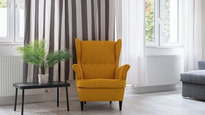 A room with a yellow armchair, a black side table with a potted plant, and a grey sofa. - RentPlanet - Apartament Mirów II (Warsaw)