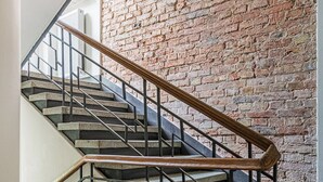A staircase with a wooden handrail and metal balusters, leading to a room with a brick wall and patterned floor tiles. - RentPlanet - Apartament Mirów II (Warsaw)