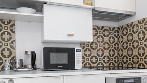 A kitchen with white cabinets, a microwave, a coffee maker, and patterned backsplash tiles. - RentPlanet - Apartament Mirów II (Warsaw)
