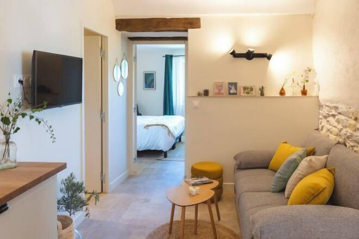 Een gezellige woonkamer met een bank, een klein tafeltje, een televisie en een deur naar een slaapkamer.