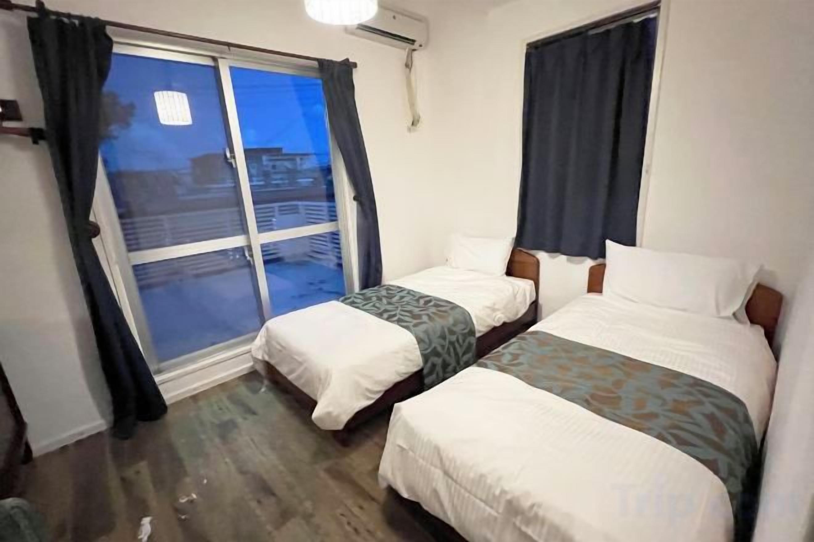 Habitación de hotel con dos camas, puerta corredera de vidrio y vistas al exterior.
