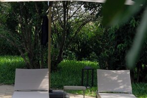 Une terrasse avec deux chaises longues et une table, entourée de verdure.
