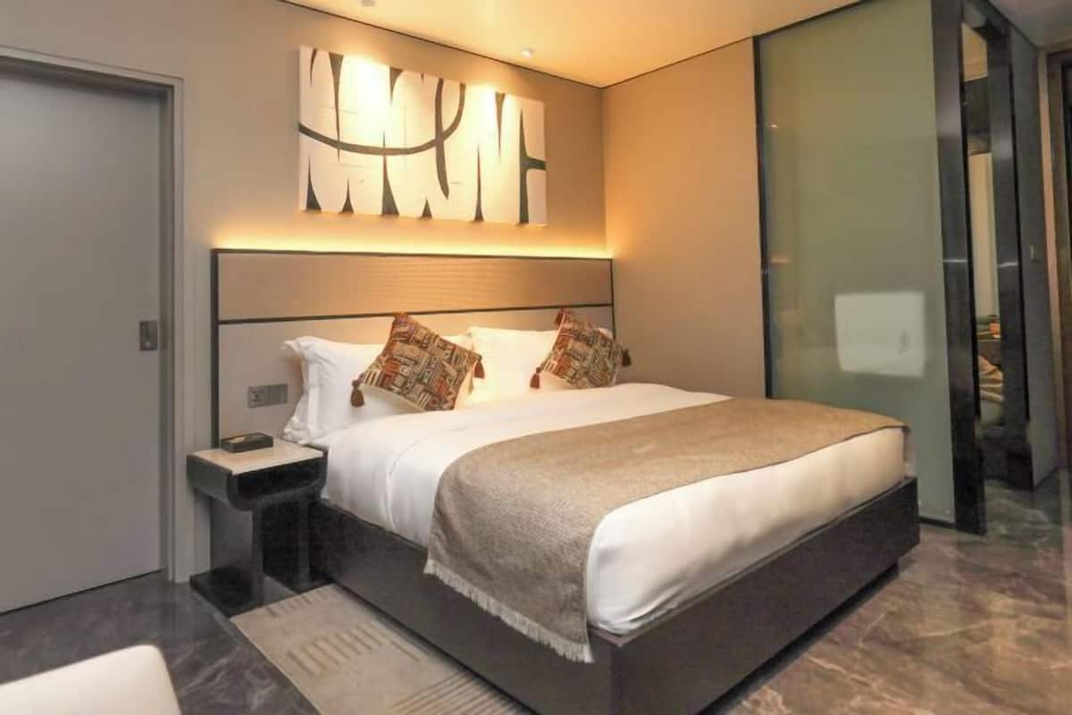 A modern bedroom with a large bed, a bedside table, and a wall-mounted abstract art piece.
