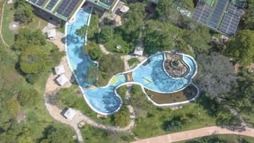 An aerial view of a resort with a large swimming pool, solar panels, and lush greenery.