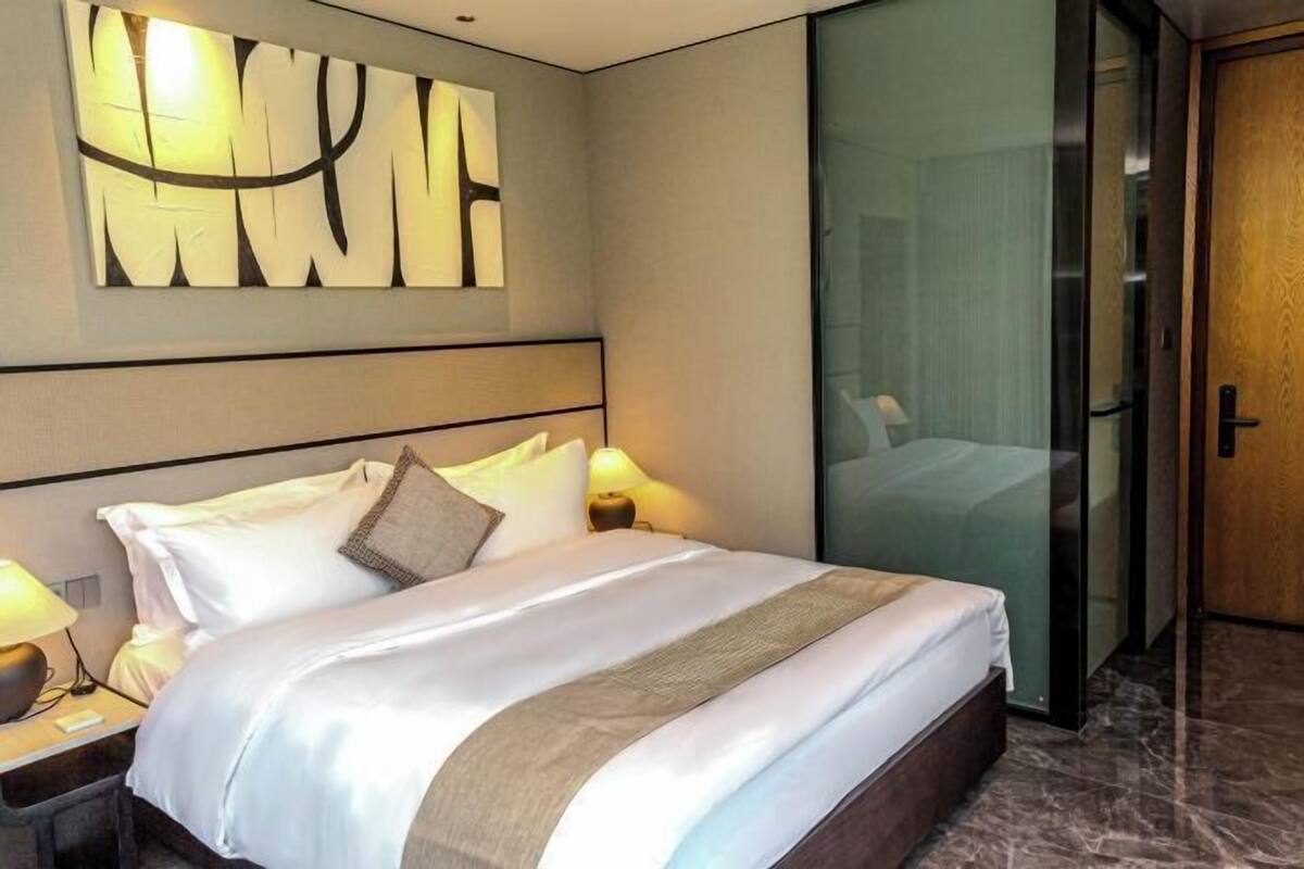 A hotel room with a large bed, bedside lamps, a wall art piece, and a sliding door to a bathroom.