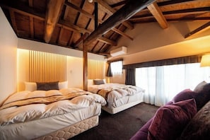 Een slaapkamer met twee bedden, houten balken in het plafond, een raam met gordijnen en een bank met kussens.