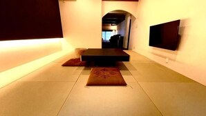 A room with tatami mats, a low table, cushions, and a flat-screen TV on the wall. - Ranjatai Premium (Nara)