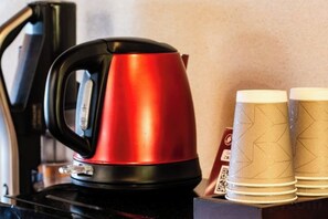 A red kettle on a black surface, possibly a table, with two paper cups with a geometric pattern beside it. - Ranjatai Premium (Nara)