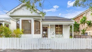 Une maison de plain-pied avec une clôture blanche en bois, une véranda et une porte d’entrée.