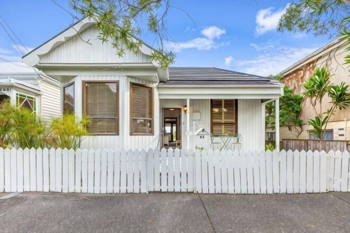 A single-story house with a white picket fence, a covered porch, and a front door.