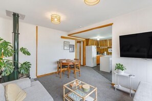 Een moderne woonkamer met een bank, een salontafel en een aan de muur bevestigde televisie. Er is een eethoek met een tafel en stoelen, en een keuken op de achtergrond.