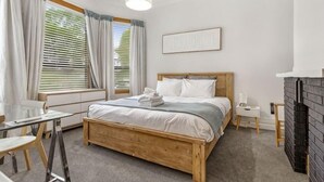 Une chambre à coucher avec un lit en bois, une table de chevet, une chaise, un bureau et une cheminée.