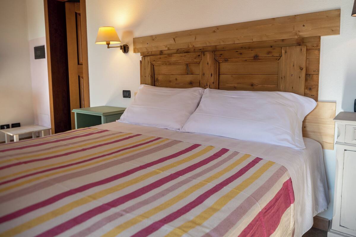 A hotel room with a wooden headboard, a striped bedspread, a nightstand, and a wall-mounted lamp.
