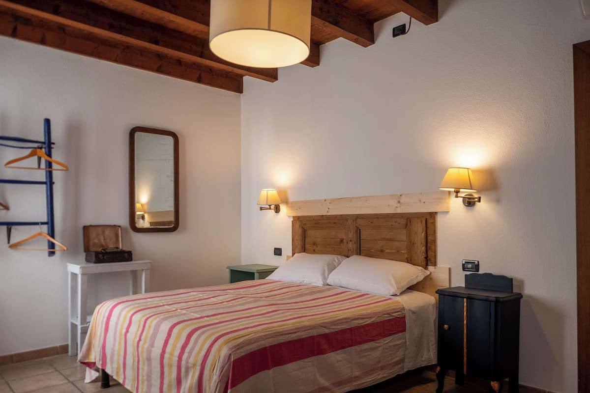 A bedroom with a wooden headboard, a bed with striped bedding, bedside lamps, a small bedside table, and a mirror on the wall.