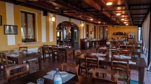 A restaurant with wooden tables and chairs, a bar area, and a view through an arched doorway. - Agriturismo Borgo del Mincio (Volta Mantovana)