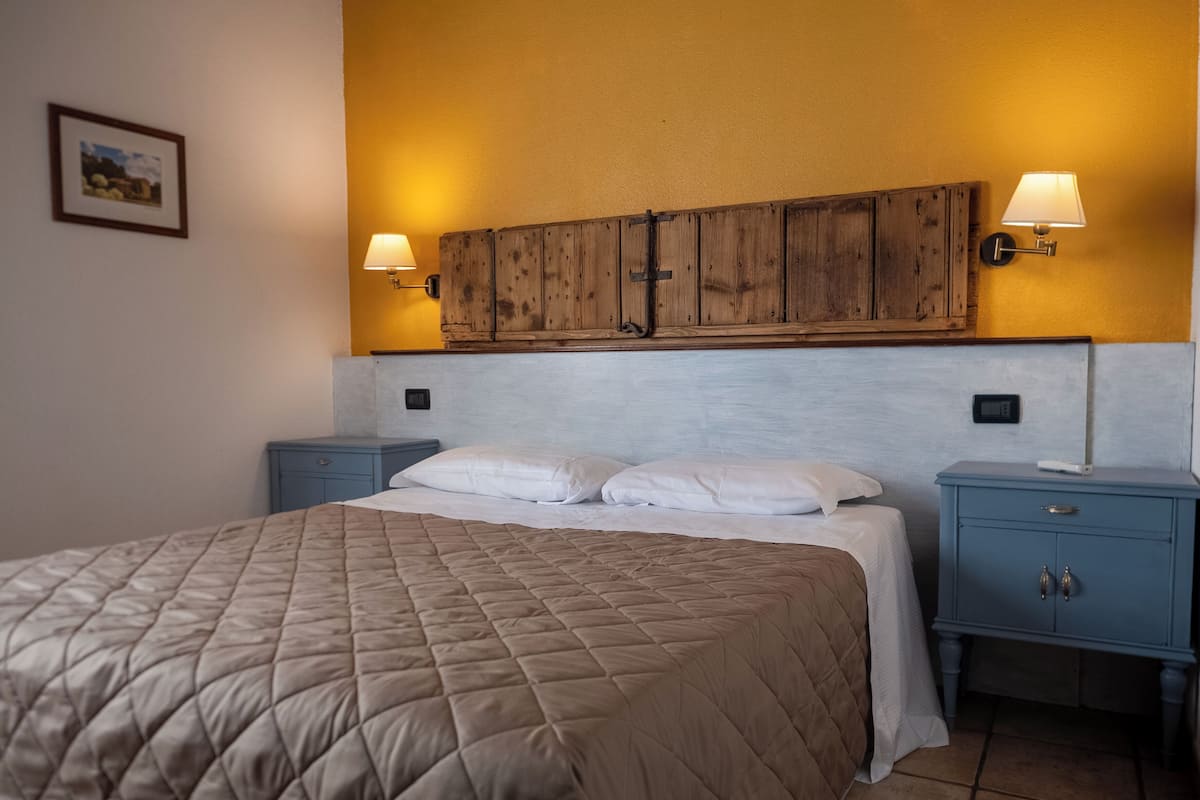 A bedroom with a large bed, two bedside tables, a wooden headboard, and wall-mounted lamps.