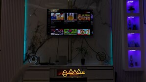 A flat-screen TV mounted on a wall with a marble-like texture, displaying various streaming content. - AM Appart's Suite Jacuzzi de luxe in Luanda (Kilamba)