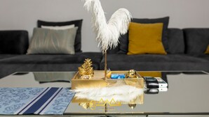 A modern living room with a glass coffee table, a decorative feather, and a golden tray with a camera. - AM Appart's Suite Jacuzzi de luxe in Luanda (Kilamba)