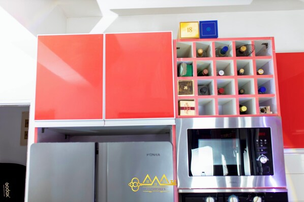 Una cocina con armarios rojos, un microondas de acero inoxidable y un almacenamiento con compartimentos numerados.