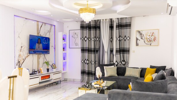 A modern living room with a large flat-screen TV, a sofa, a coffee table, and decorative pillows. - AM Appart's Suite Jacuzzi de luxe in Luanda (Kilamba)