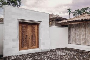 A building with a large wooden door, a white exterior wall, and a thatched-roof structure. - Villa La Canopee by BaliSuperHost (Bali)