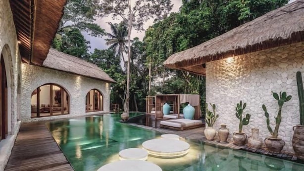 A pool area with a wooden deck, a thatched-roof structure, and a stone wall with potted plants. - Villa La Canopee by BaliSuperHost (Bali)